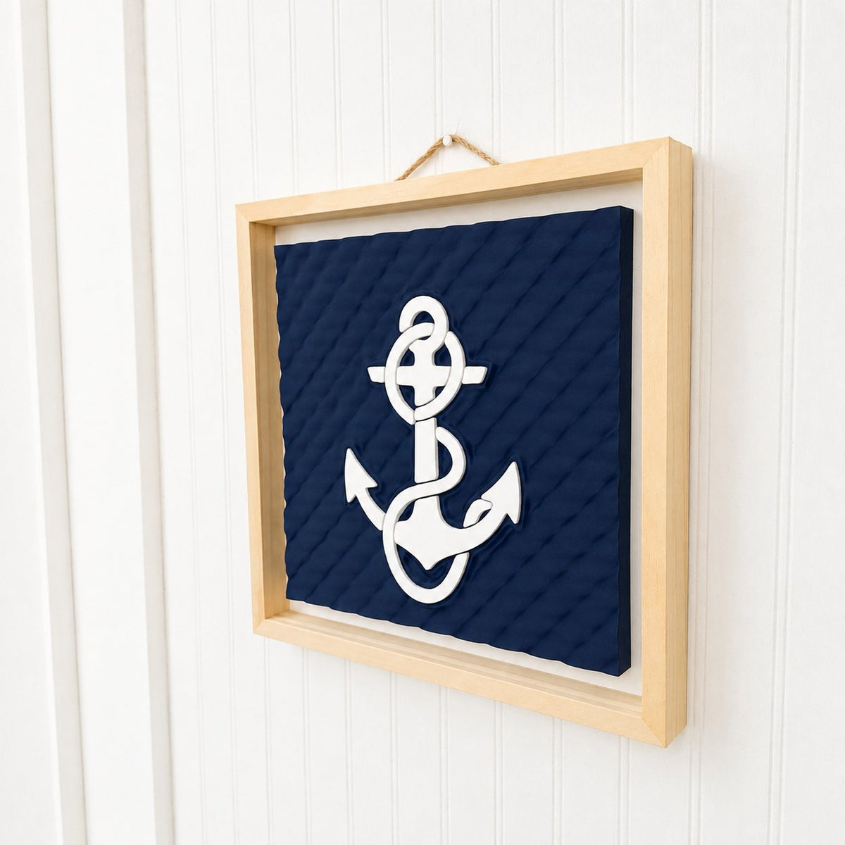 Framed anchor wall art hanging on a white shiplap wall with its jute rope hanger