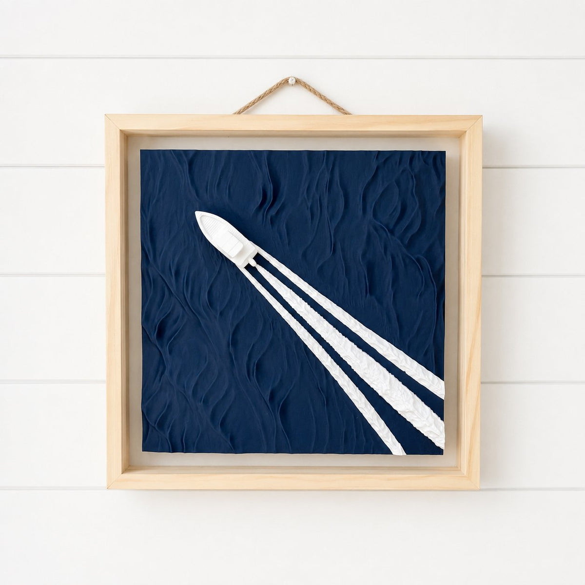 Framed 3D boat wake wall art hanging by a jute rope on a white shiplap wall