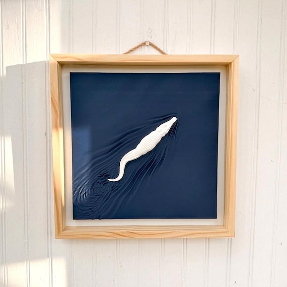 White alligator and sculpted wake on a navy panel, in a natural pine frame.