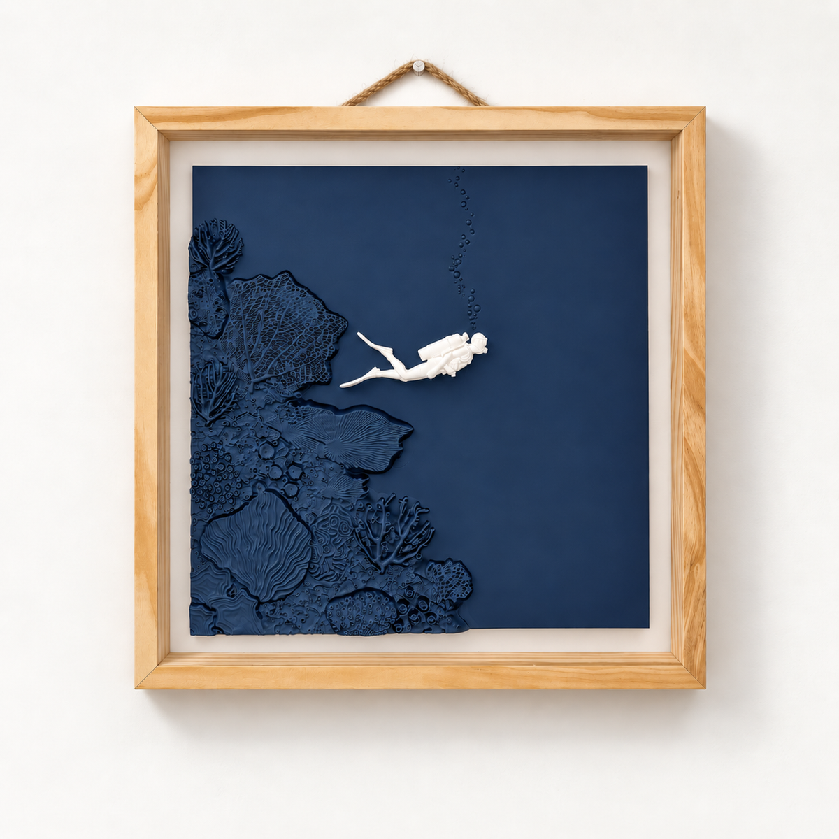 Scuba diver wall art, front view of a bone-white diver beside sculpted navy coral in a natural wood frame